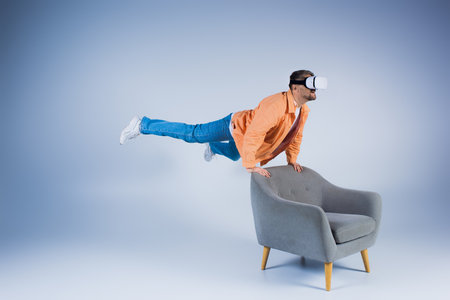 A man in an orange shirt executes a mesmerizing trick on a chair in a studio setting, showcasing his magic skills.の写真素材