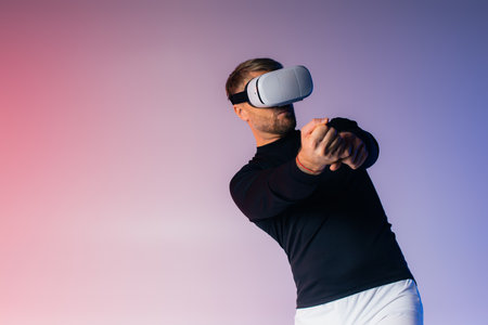 A man in a VR headset swings a baseball bat while blindfolded in a studio setting, showcasing virtual reality sports training.の写真素材