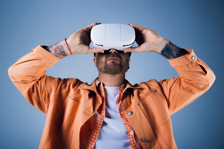 A man in an orange shirt raises a white vr headset above his head in a studio setting.の写真素材