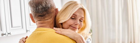 A mature loving couple in cozy homewear, the woman embracing the man in a yellow sweater in a warm,...