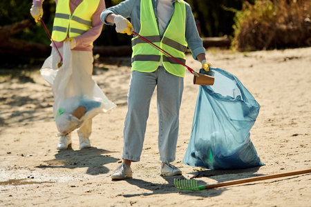 A couple in safety vests and gloves stands in the sand, united in cleaning a park together.の写真素材