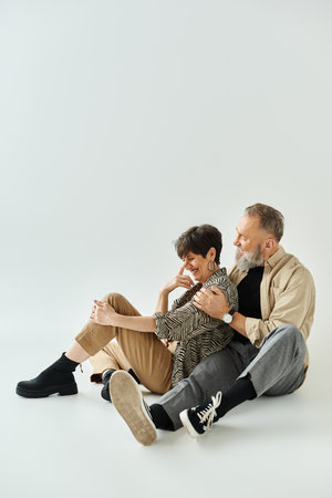 A middle-aged couple in stylish attire seated closely together in a studio setting, exuding sophistication and unity.の写真素材