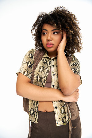 beautiful african american woman in clothes with animalistic print on white backdrop looking away