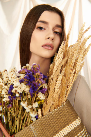 A young woman with long brunette hair, exudes a summer vibe as she holds a bouquet of dried flowers in a studio setting.の写真素材