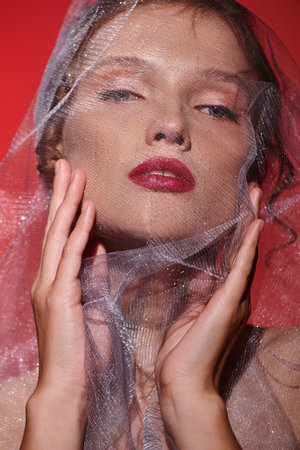 A young woman exudes timeless beauty in a studio setting, her head adorned with a delicate veil on a...
