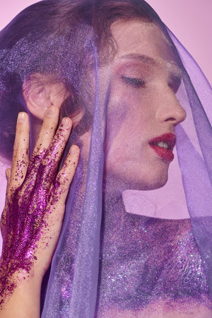 A young woman exudes classic beauty as she poses in a studio setting, her face delicately adorned with purple makeup and a veil covering her head.の写真素材