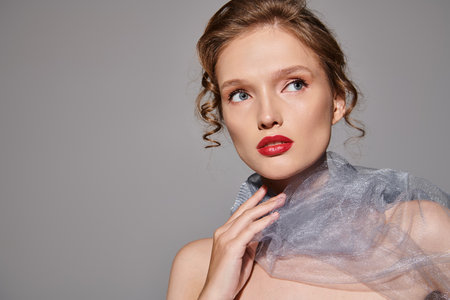 A young woman exudes classic beauty as she poses in a studio, wearing a veil and striking red...