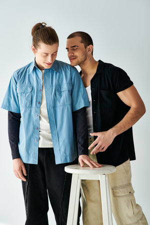 Two men stand near a stool, sharing a moment of closeness.