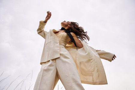 A beautiful young woman in a white suit is gracefully flying through the air, embracing the summer breeze in a serene field.の写真素材