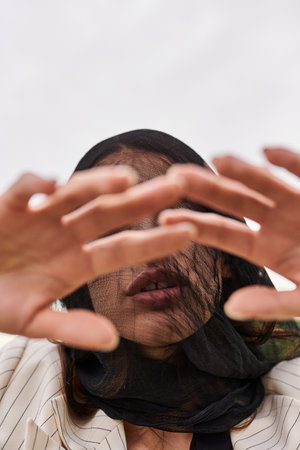 A young woman in white attire, her face covered by a veil, enjoying the summer breeze in a field of nature.の写真素材