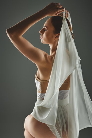 A young woman in a white dress gracefully holds a white scarf over her head.の写真素材