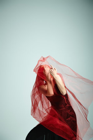 Young ballerina in a black dress gracefully dances with a veil on her head.