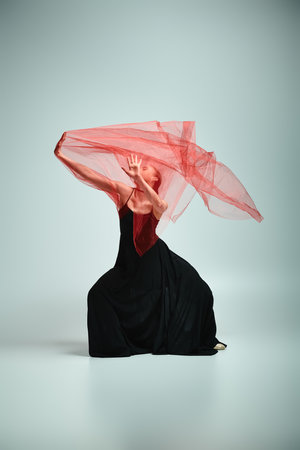 A graceful ballerina in a striking black dress moves elegantly with a red veil on her head.の写真素材