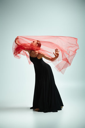 A young beautiful ballerina in a flowing black dress and vibrant red scarf dances gracefully.の写真素材