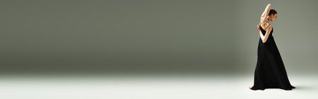 A young woman in a long black dress gracefully raises her hands in a ballet pose.の写真素材