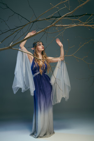 A young woman dressed in blue and white holds a delicate branch, embodying a fairy princess in a whimsical setting.の写真素材