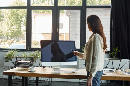 A businesswoman stands confidently in front of a computer screen in a modern office, immersed in the world of franchise concepts.の写真素材