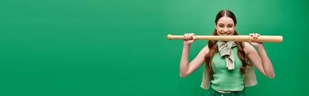 A young, beautiful woman in her 20s holds a baseball bat in front of her face in a studio setting on green.の写真素材