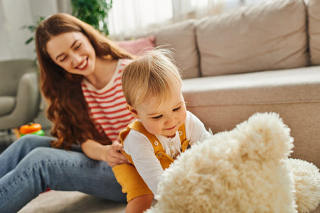 A young mother sits on the floor next to her little baby girl, engaging in a loving moment of togetherness and bonding.の写真素材