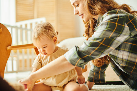 A young mother joyfully interacts with her toddler daughter while playing together on the floor at...