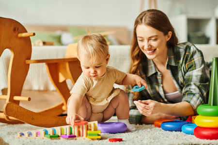 A young mother joyfully playing with her baby daughter on the cozy floor of their home.の写真素材