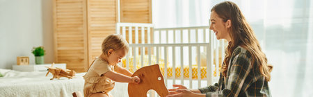 A young girl joyfully plays on a wooden rocking horse while her mother watches with a smile.の写真素材