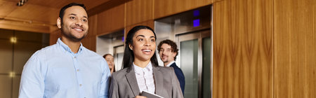 A man and a woman, an interracial group of business professionals, stand in front of an elevator.