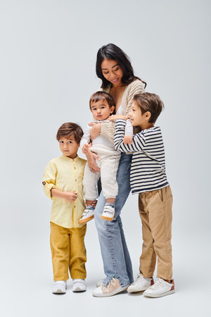 A young Asian mother tenderly holding her children, stand close by in a studio setting against a...