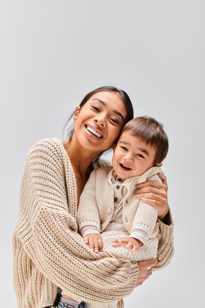 A young Asian mother tenderly holds her child in her arms against a soft grey studio backdrop.の写真素材