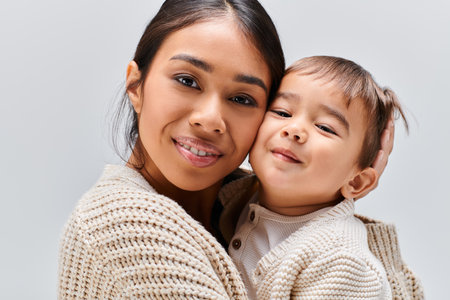 A young Asian mother tenderly holds her child in her arms in a studio setting against a grey background.の写真素材