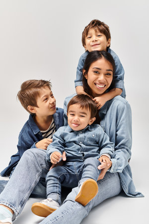 A group of people, a young Asian mother and her little sons, sitting on top of each other in a grey studio, all wearing denim clothes.の写真素材