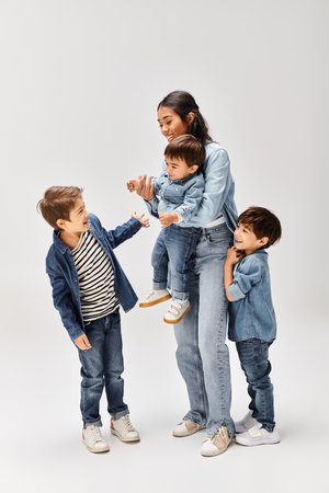 A young Asian mother and her little sons, dressed in denim, having a playful and joyful time together in a grey studio.の写真素材