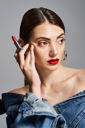 A young Caucasian woman with brunette hair in a denim dress holding a red lipstick.の写真素材