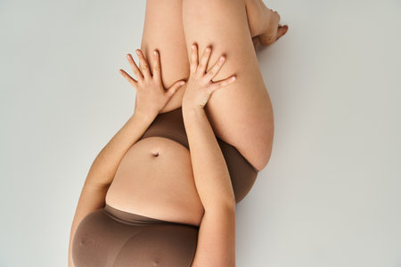 cropped shot of body plus size young girl in brown underwear with hands on thighs on grey backgroundの写真素材