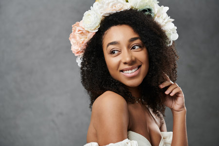 A beautiful African American bride wearing a white wedding dress and a flower crown smiles while standing in front of a grey background.の写真素材