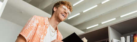 A man laughs while holding a book in a library.の写真素材