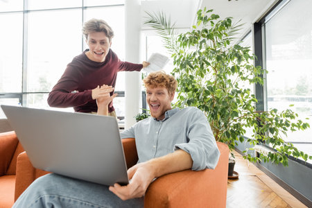 Two male students work together on a laptop while sitting on a couch.