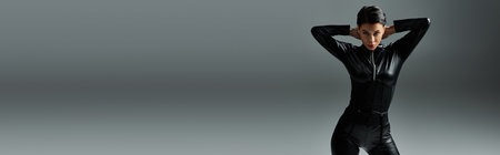 A woman in black leather jumpsuit poses seductively against a grey background.の写真素材