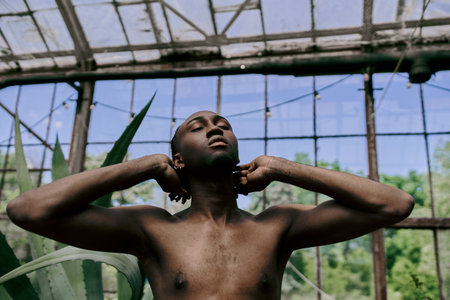 An elegant African American man standing by a window, hands on ears.