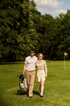 A graceful young couple in elegant attire enjoying a leisurely walk on a picturesque golf course surrounded by lush greenery.の写真素材