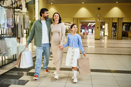 A happy family with shopping bags walks through a bustling mall on a fun weekend outing together.の写真素材
