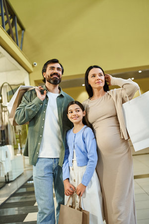 A family happily carries shopping bags while strolling through a bustling mall on a weekend outing.の写真素材