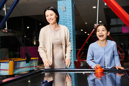 A mother and her daughter joyfully playing air hockey in an arcade during a fun weekend outing at the mall.の写真素材