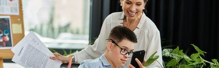 A mother smiles at her son as they work side-by-side in a modern office, showcasing inclusion and...