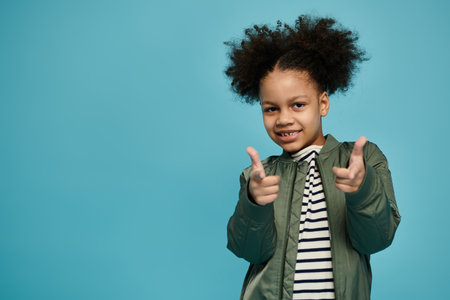 A young African American girl with curly hair smiles and points towards the viewer in a studio setting.の写真素材