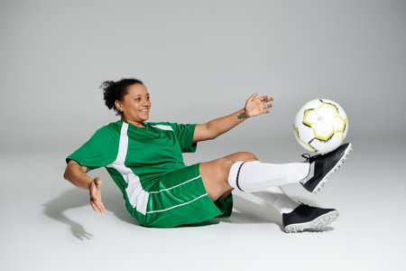 A woman wearing a green jersey and shorts juggles a soccer ball with her foot.の写真素材