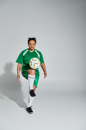 A woman in a green jersey skillfully juggles a soccer ball in a studio setting.の写真素材