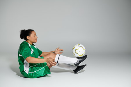 Woman in green soccer uniform gracefully balances ball on outstretched foot.の写真素材