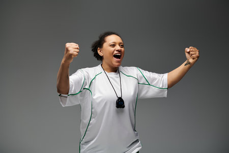 Female athlete rejoices on field after victory, joy evident in raised fists and wide grin.の写真素材