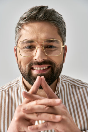 A bearded man in glasses and a striped shirt poses elegantly on a grey background in a studio setting.の写真素材